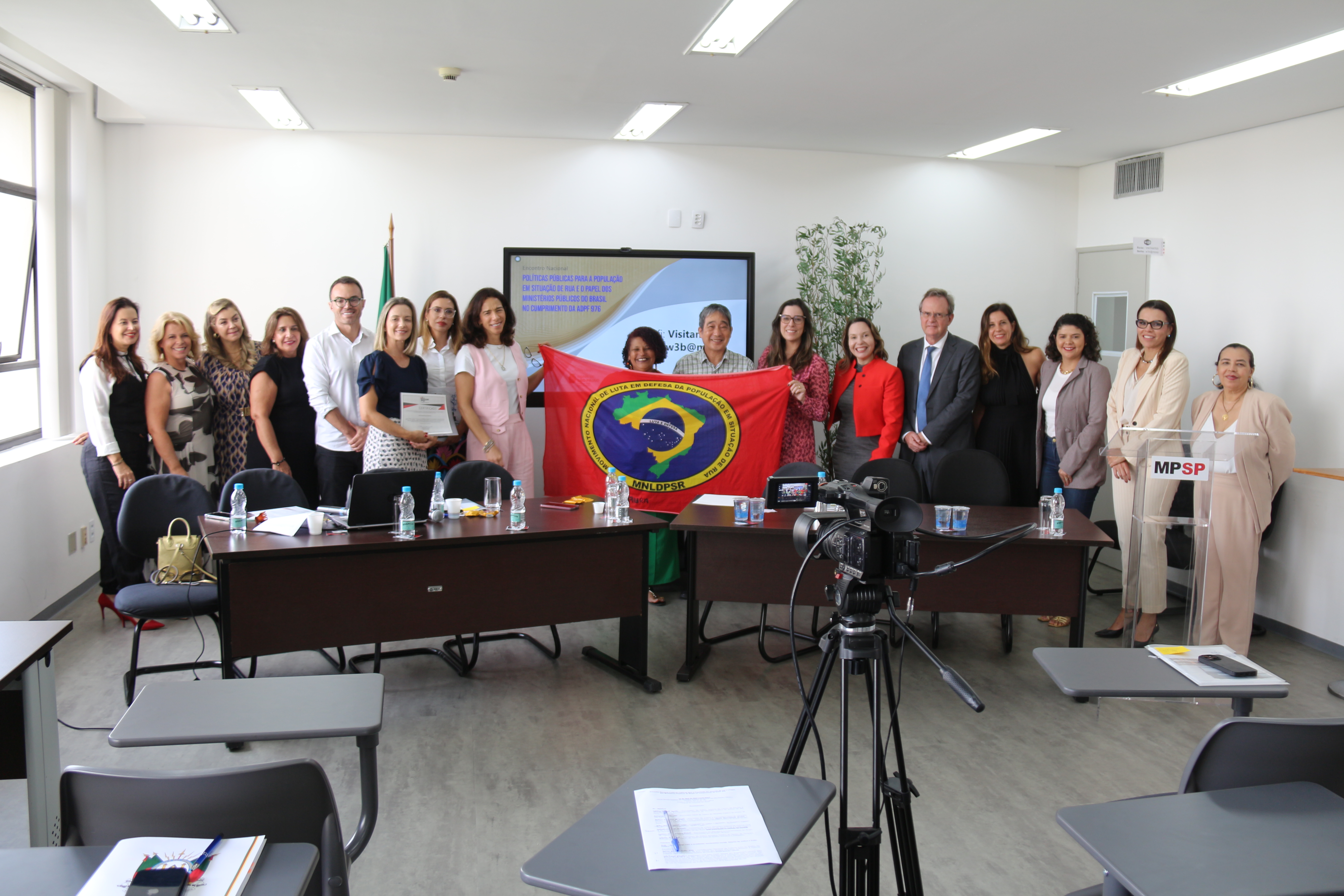Foto com participantes do evento e, ao centro, a bandeira do Movimento Nacional de Luta em Defesa da População em Situação de Rua