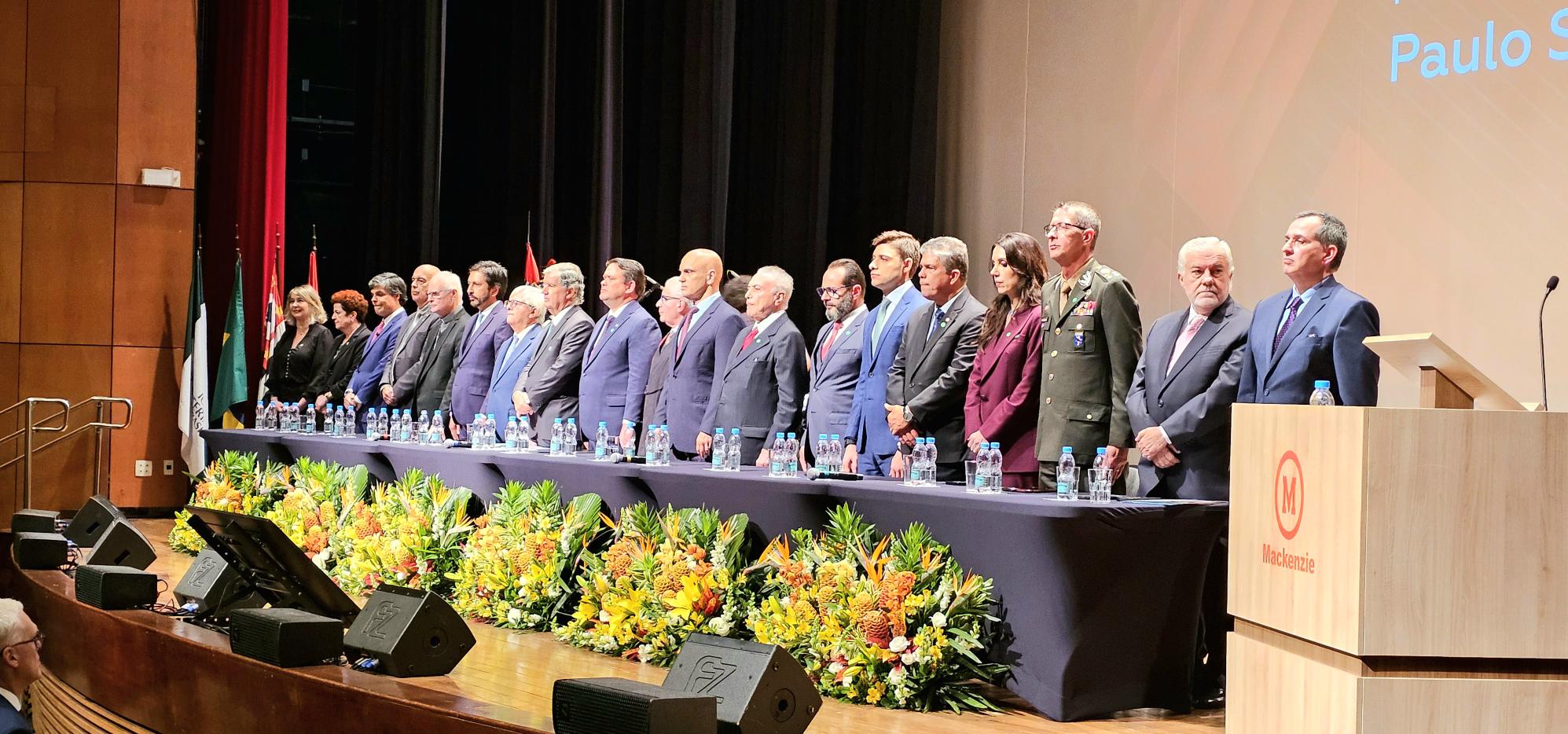 Foto mostra participantes à mesa de honra da solenidade. Fim da descrição.