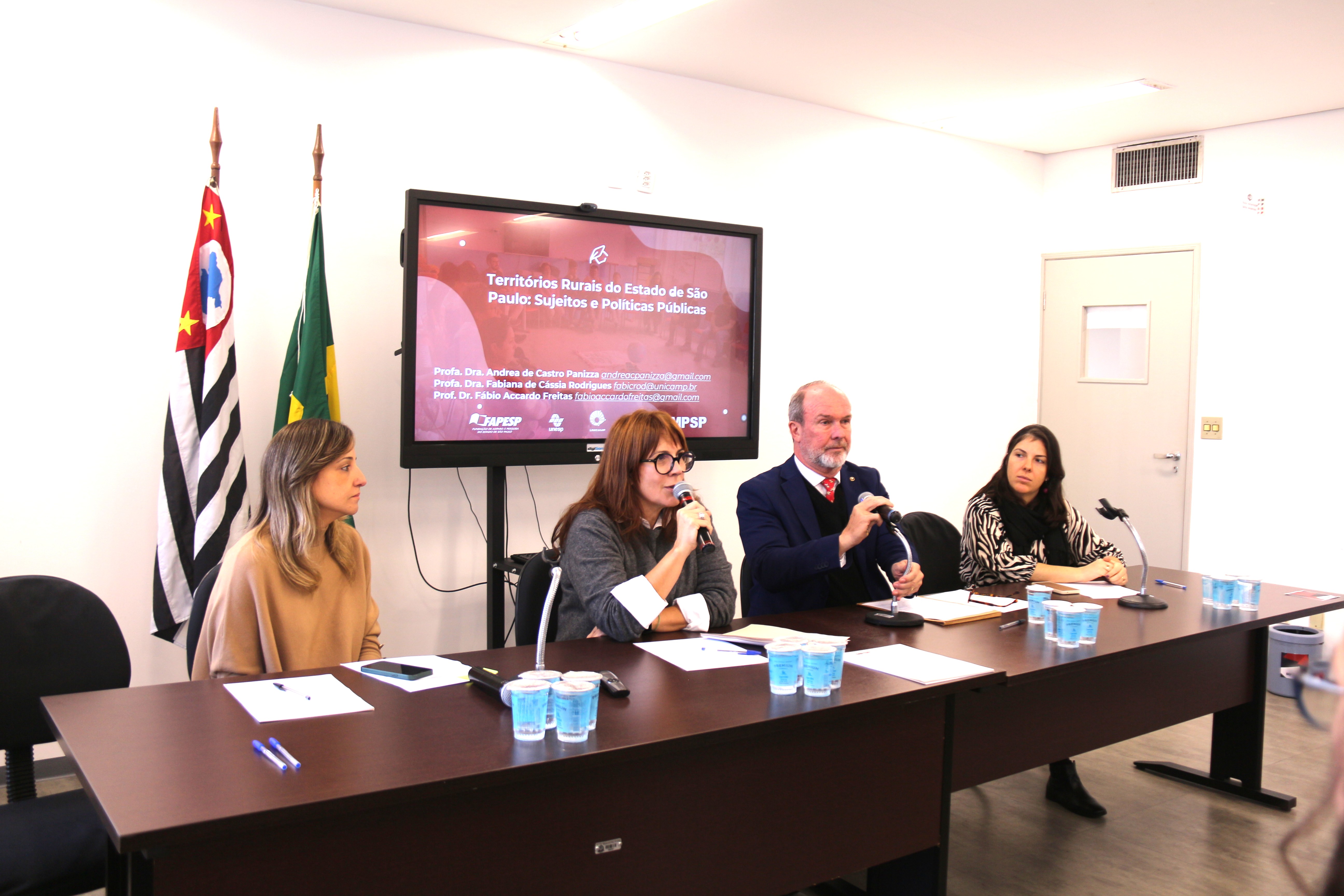  foto mostra participantes à mesa de debates. Fim da descrição.