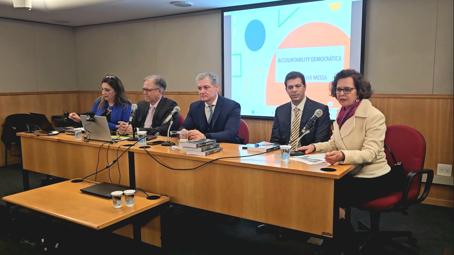 Foto mostra a diretora da ESMPSP e palestrantes no evento. Fim da descrição. 