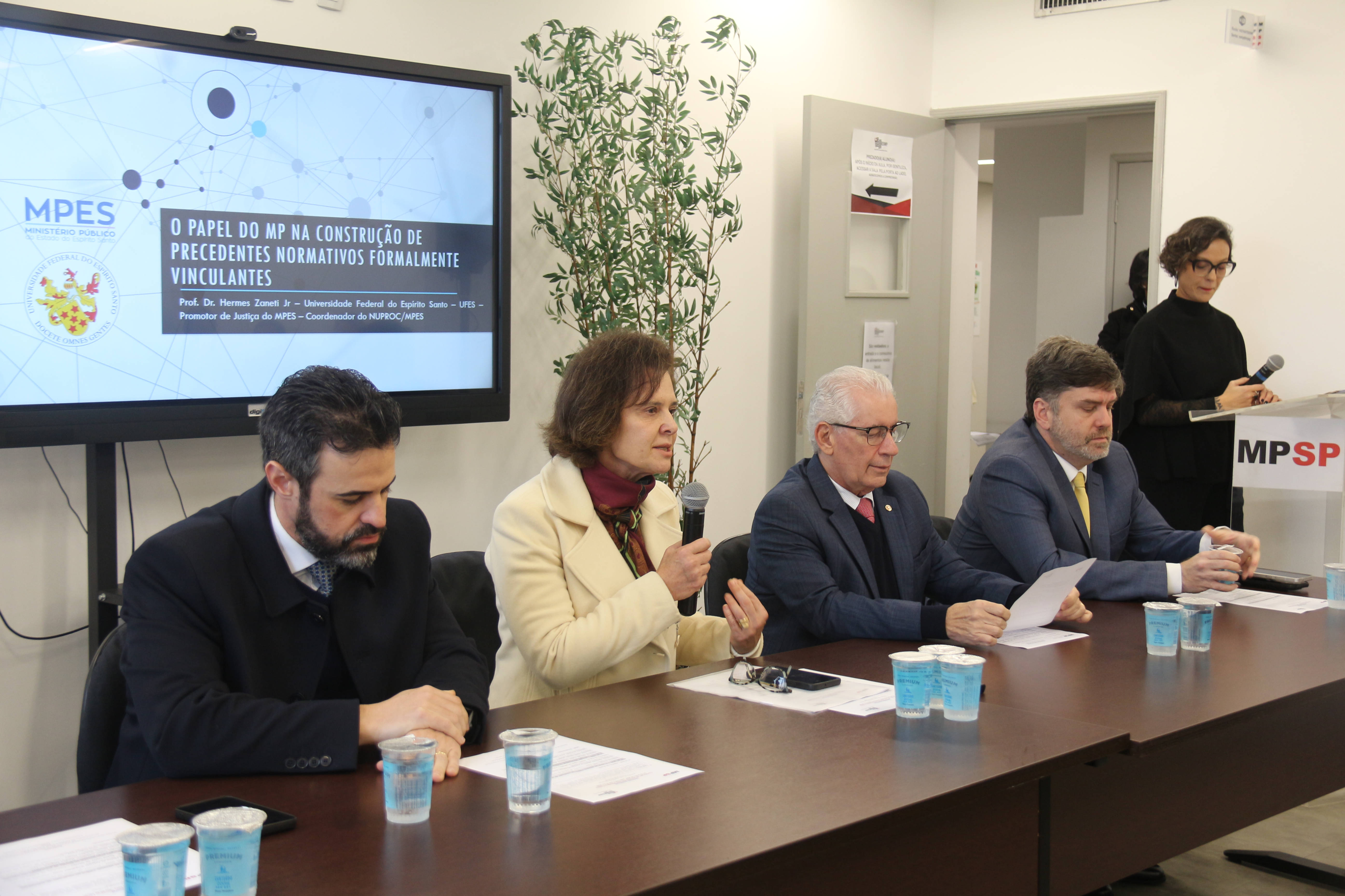Foto mostra participantes à mesa de debates durante o evento. Fim da descrição.   
